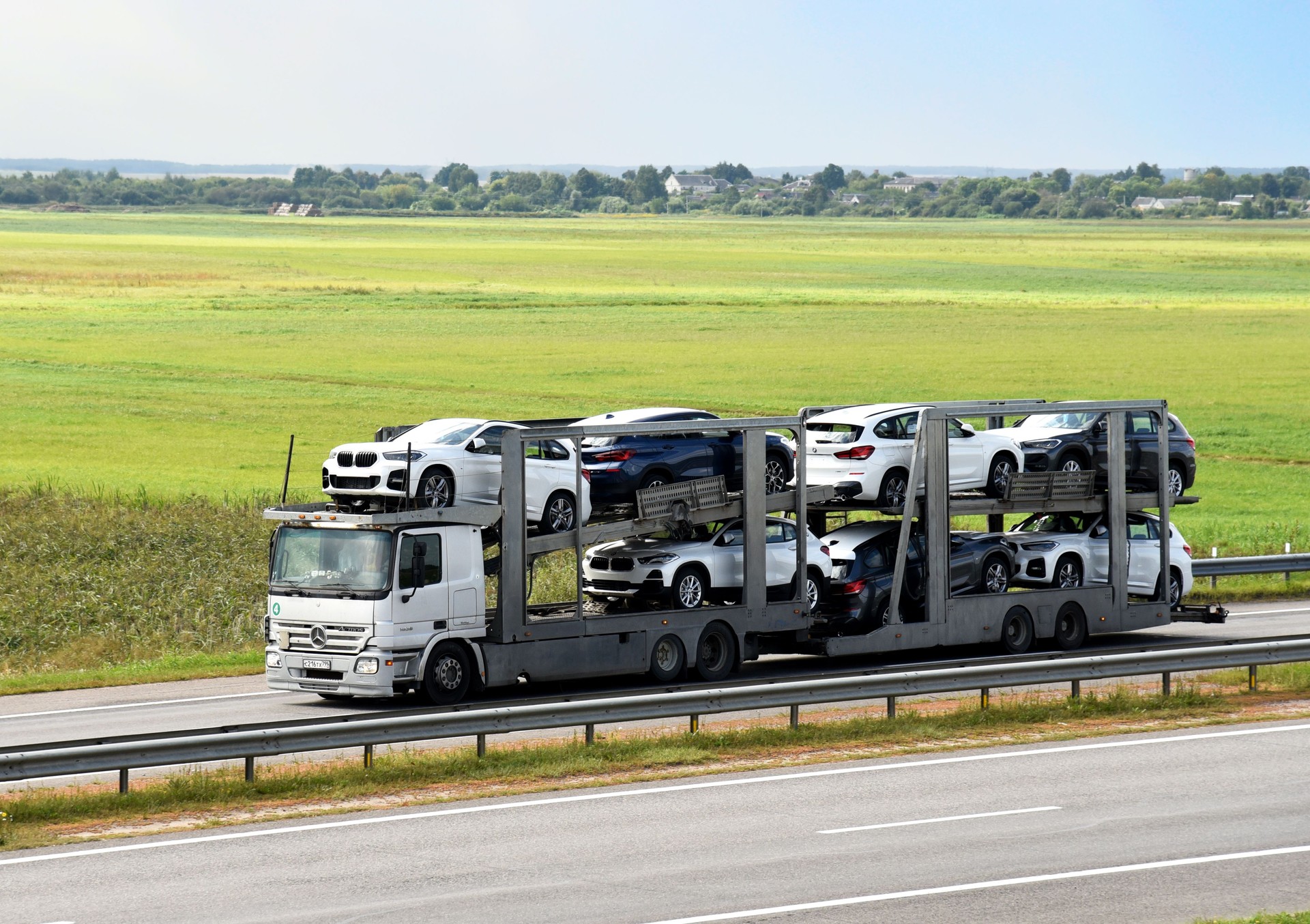 Car carrier trailer transports BMW X1 cars on highway.