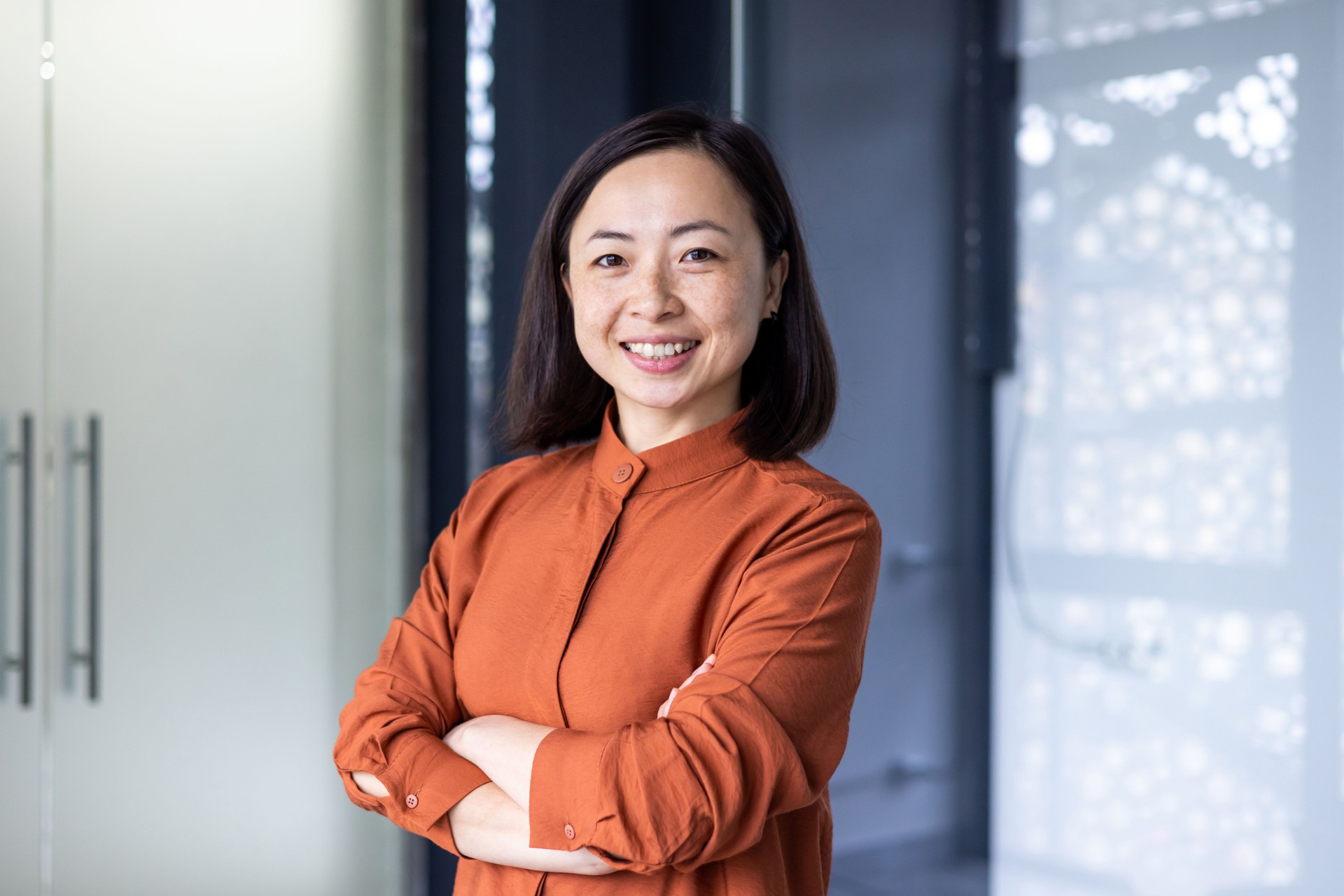 Portrait of young beautiful and successful Asian business woman, female employee smiling and looking at camera with crossed arms, financial woman satisfied with the results of her work achievement