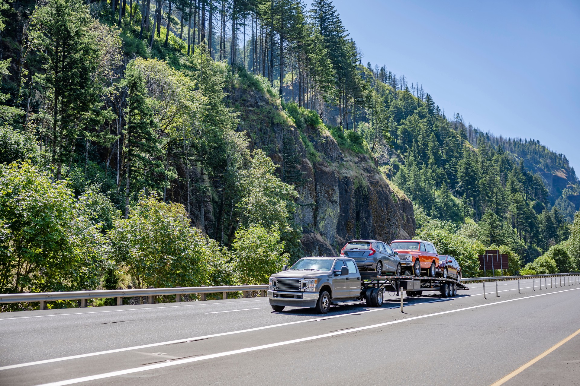 Compact truck transporting cars on the small semi trailer running on the scenic highway road with forest and mountain